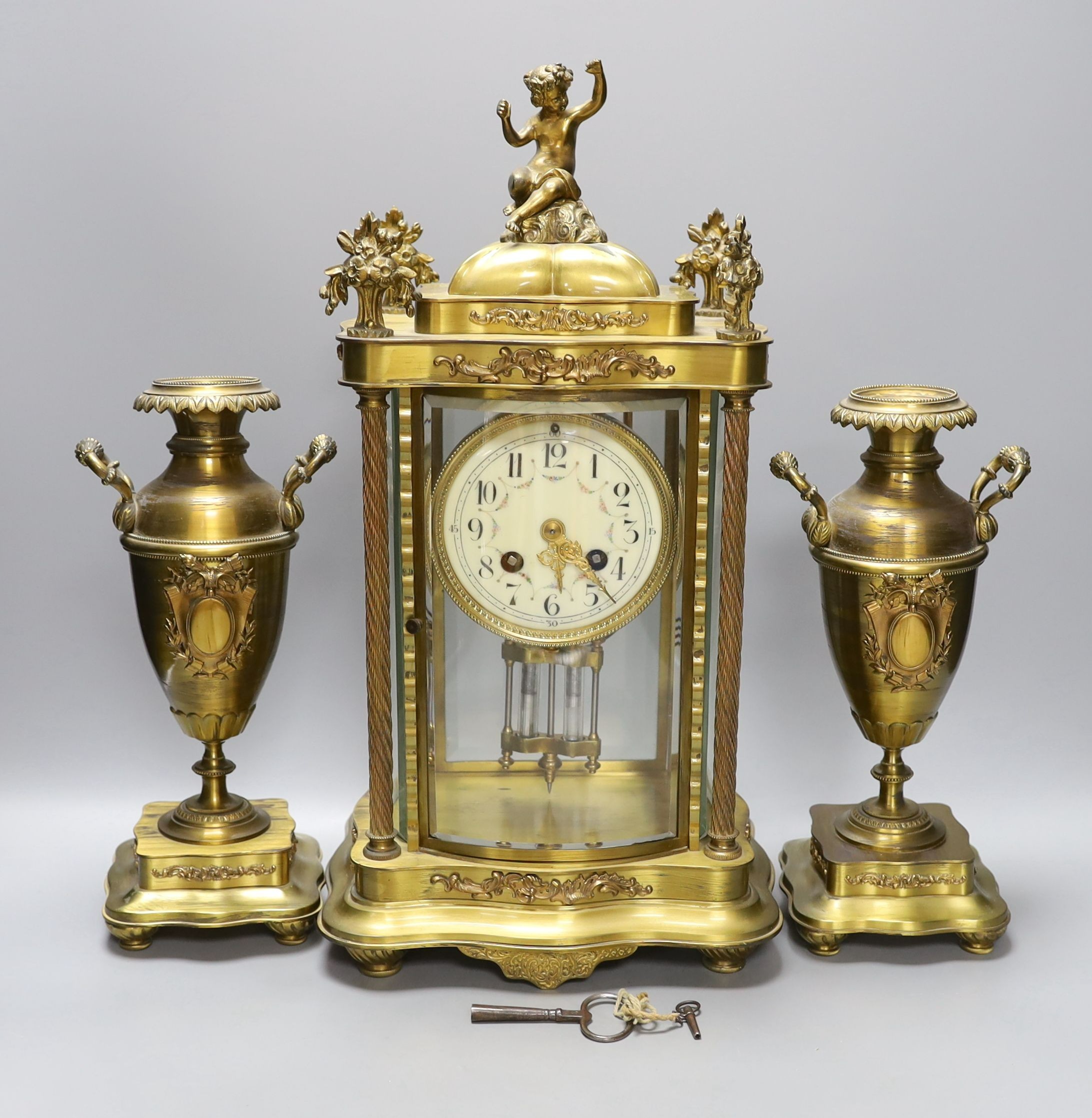 An early 20th century French brass four glass mantel clock garniture with key and pendulum, 41cm tall